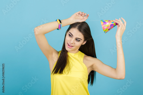 young attractive smiling woman with birthday hat and whistle on blue background. celebration and party