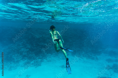 Underwater photo of woman snorkeling and free diving in a clear tropical water at coral reef