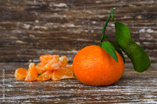 Close up of whole mandarin with green leaves and mandarin slice on wood table. Organic tangerine fruit background with copy space.