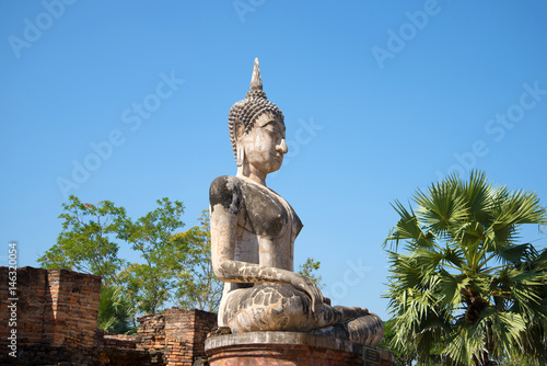 A view of the ancient sculpture of a sitting Buddha on the ruins of the Buddhist temple of Wat Mae Chon on a sunny afternoon. Sukhothai  Thailand