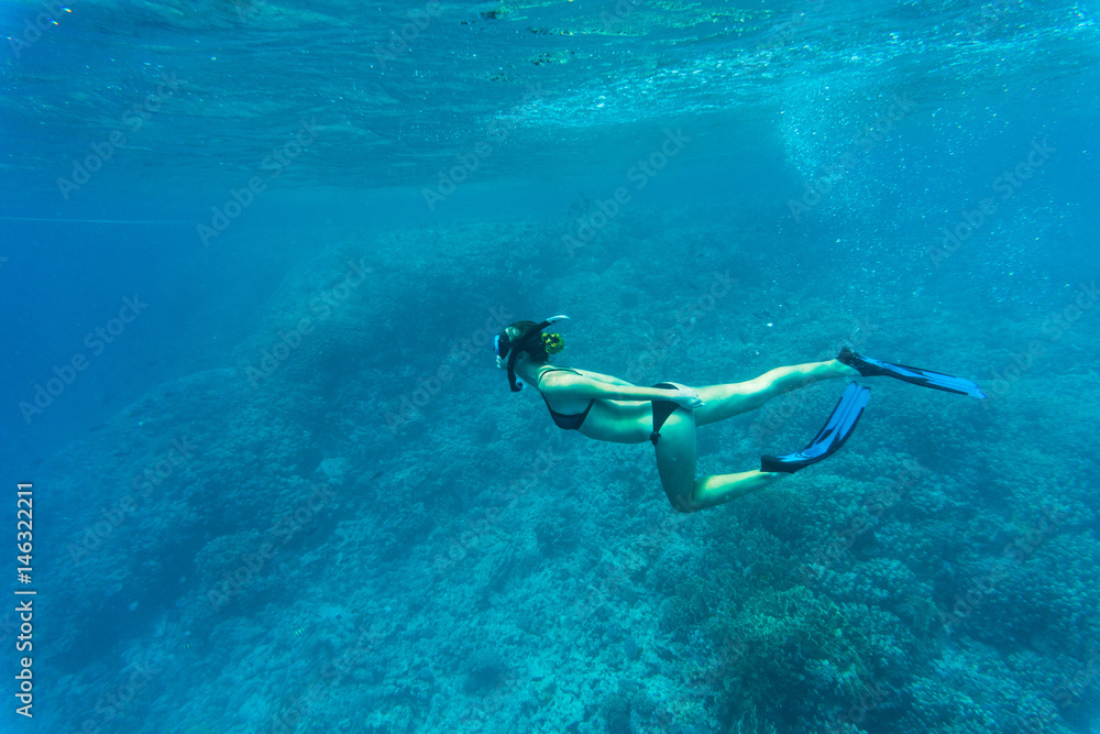 Free woman diver gliding snorkeling underwater over vivid coral reef in a tropical sea