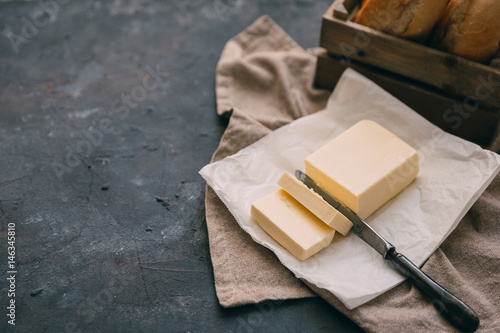 Pat of fresh farm butter  with a knife and bread over rustic background