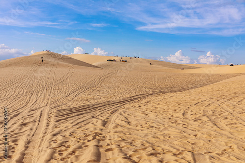 Sand dunes near Mui Ne. Group of jeeps on top of dunes in the background. Sunny day with blue sky and clouds.