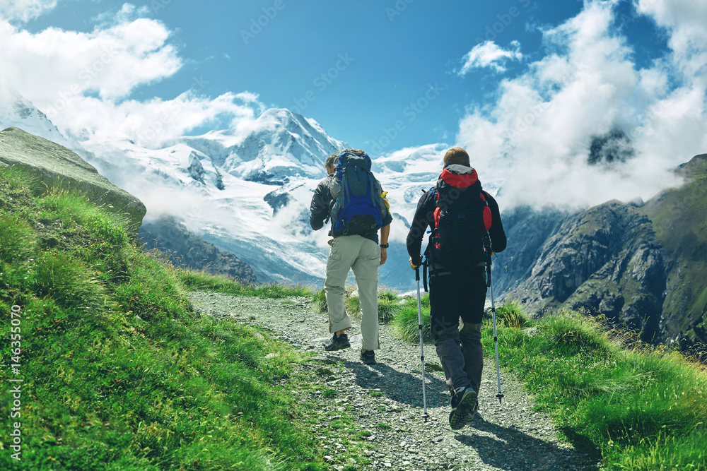 hikers with backpacks on the trail in the Apls, Swiss mountains. Trek near Matterhorn mount, mountain ridge on background