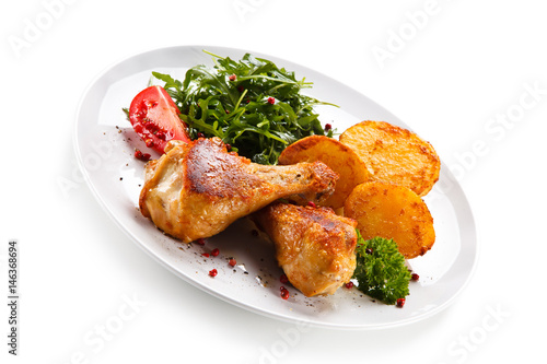 Roast chicken drumsticks with potatoes on white background