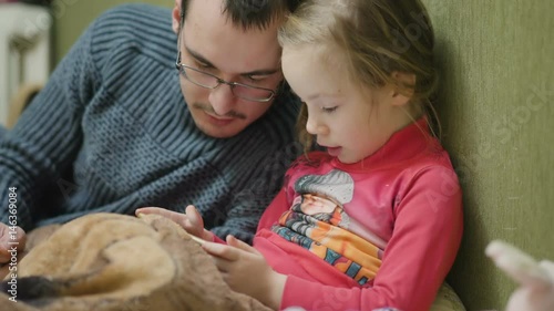 Young child girl with father playing game on mobile phonein dark room, photo