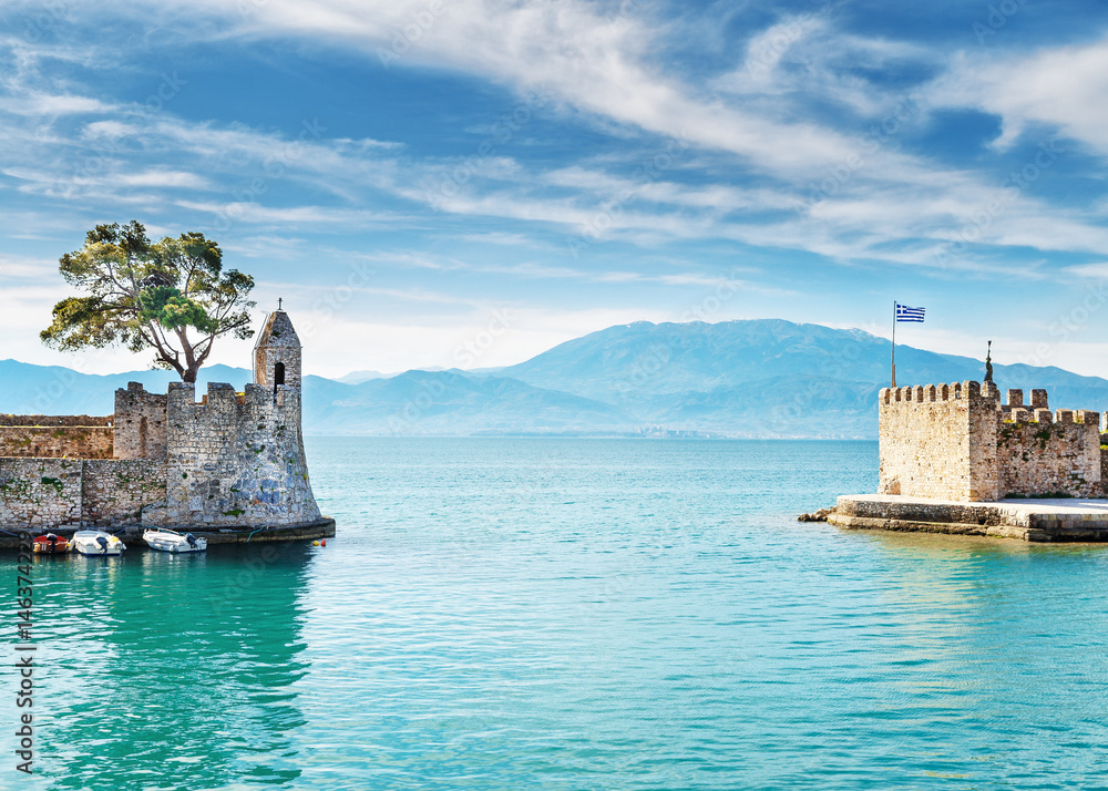 Amazing morning scenery of old port gate in Nafpaktos town, Western Greece, nearby Patras city. Beautiful dramatic blue sky at background. Turquoise water of Ionian sea. Vintage style scenery.