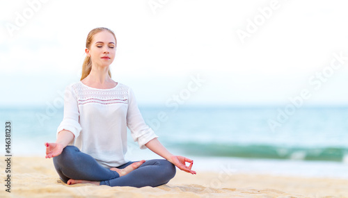woman practices yoga and meditates in lotus position on beach.