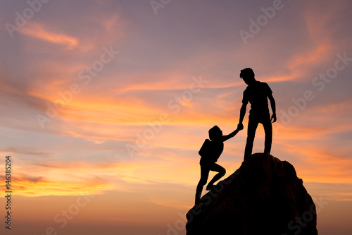 Фотография Teamwork couple hiking help each other trust assistance silhouette in mountains, sunset