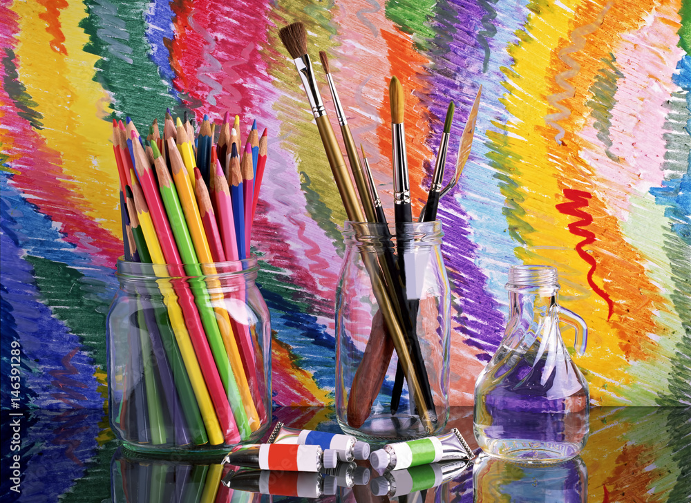 Fototapeta premium On a glass dark table are banks with colored pencils and brushes for drawing