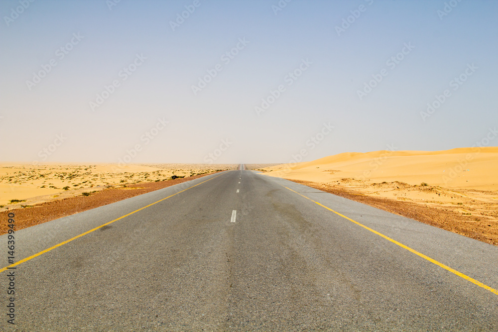 Well paved and seemingly endless road leading through dunes in the dry and hot desert are part of the transportation infrastructure of the Sultanate of Oman on the Arabian peninsula in the Middle East