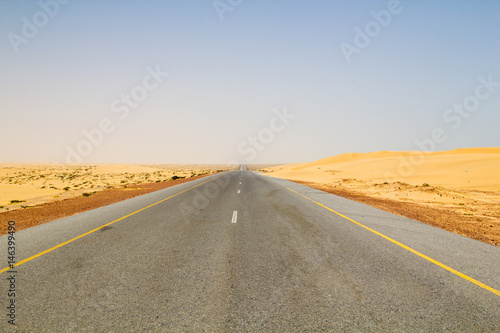 Well paved and seemingly endless road leading through dunes in the dry and hot desert are part of the transportation infrastructure of the Sultanate of Oman on the Arabian peninsula in the Middle East