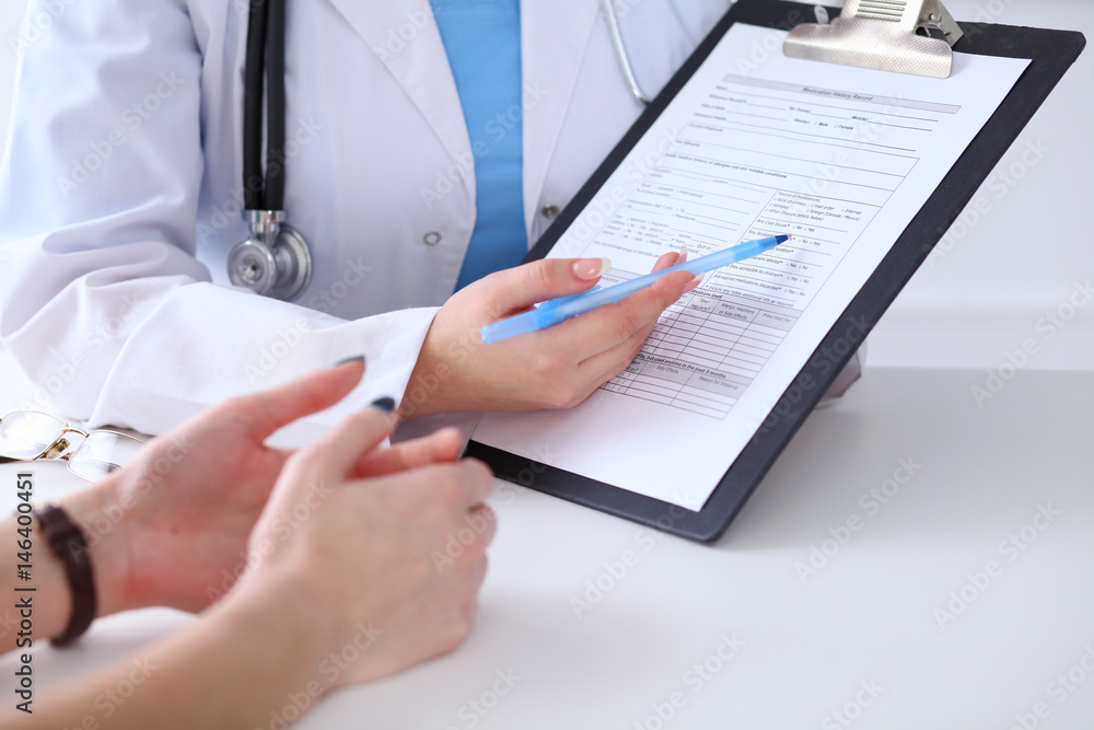 Close up of a doctor and patient hands while phisician pointing into medical history form at clipboard. Medicine and health care concept Close up of a doctor and patient hands while phisician pointing into medical history form at clipboard. Medicine and health care concept