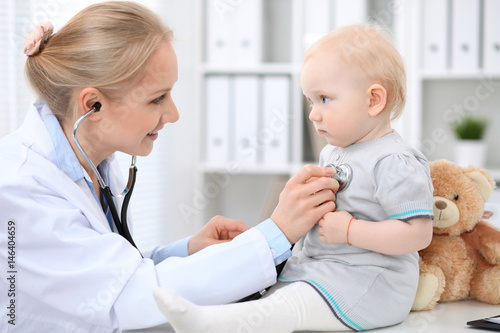 Pediatrician is taking care of baby in hospital. Little girl is being examine by doctor with stethoscope. Health care, insurance and help concept.