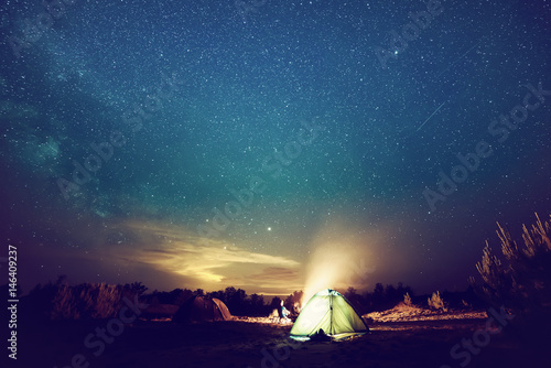 Camping fire under the amazing blue starry sky with a lot of shining stars and clouds. Travel recreational outdoor activity concept. © Roxana