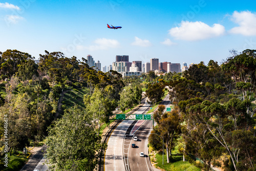 An airplane flies over the Cabrillo Freeway (State Route 163) as it passes through Balboa Park and into the downtown area of San Diego, California.  