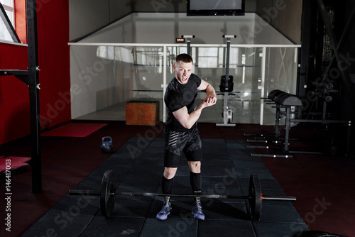 Screaming young man dressed in black t-shirt showing his biceps in gym. Man posing in gym and looking at camera while showing his biceps