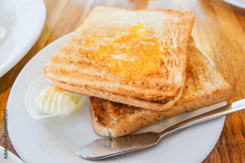 Bread toast with orange jam, cream and the knife steel serve on white dish for food background.
