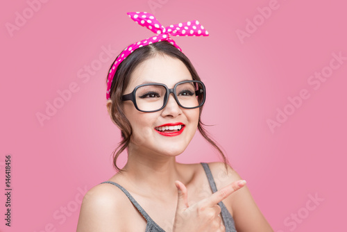 Young asian with pin-up make-up pointing to space over pink background.