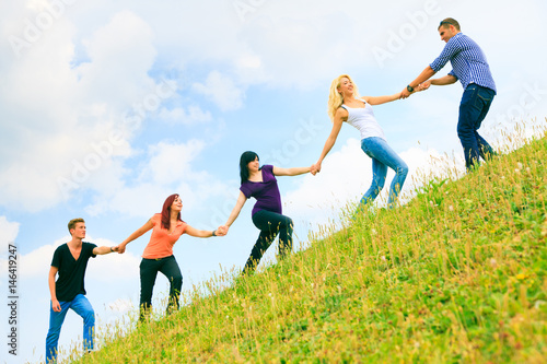 Young People Helping Each Other Climb A Hill