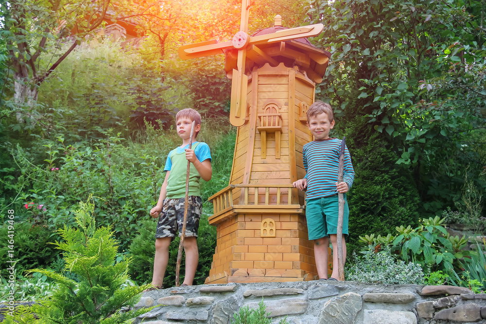 Obraz premium Two boys next to small mill in summer city park in sunlight