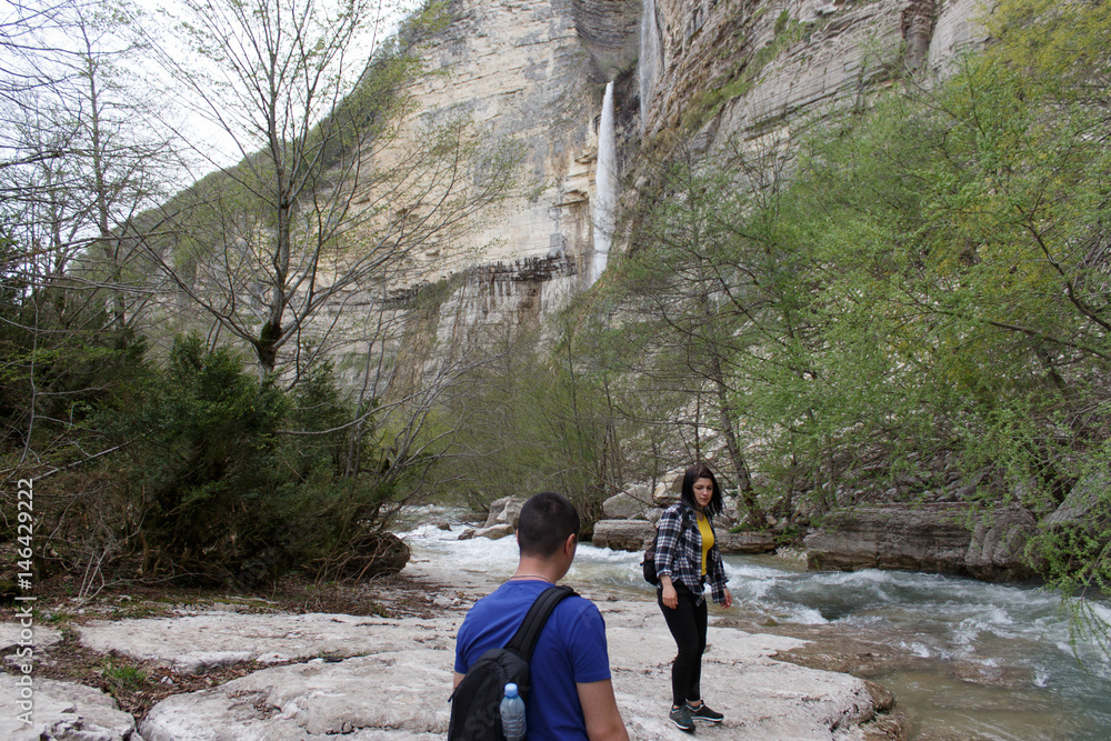 Traveler young girl and men walking in waterfall canyon. Travel adventure and hiking activity