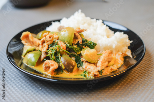 Green curry pork in coconut milk with eggplant and steamed rice serve on black plate.