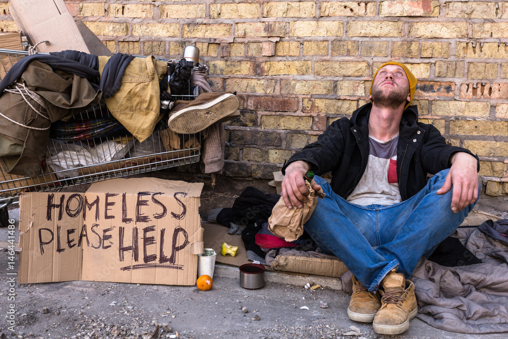 Poor homeless man with cart. Sitting near the wall and looking at the