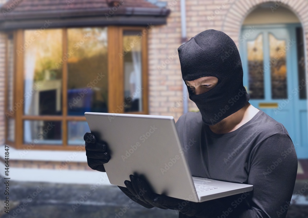 Criminal in hood on laptop in front of home house Criminal in hood on laptop in front of home house
