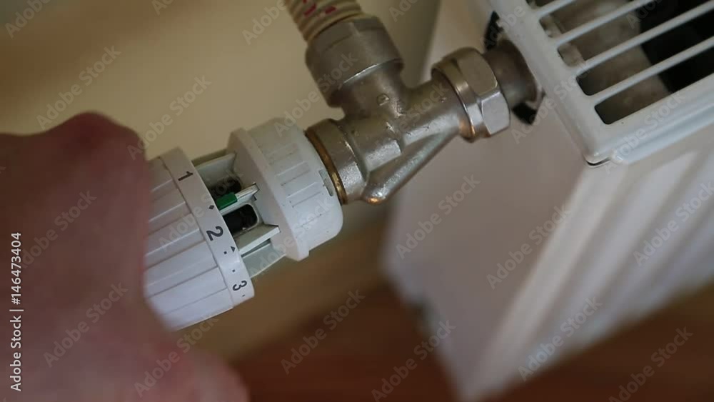 Man adjusts the temperature of the battery. Central heater with temperature controller. Heating battery with temperature regulator, house heating system Man adjusts the temperature of the battery. Central heater with temperature controller. Heating battery with temperature regulator, house heating system