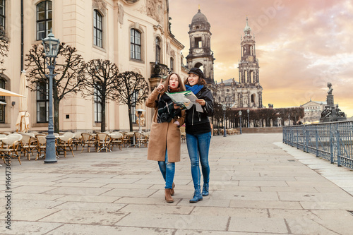 Two charming cheerful women are walking with a map along Dresden Street, Germany. The concept of love and friendship in travel photo