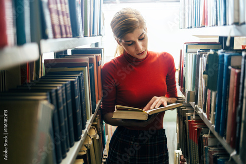 Young woman reading a book in library photo