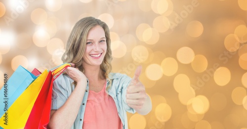 Woman showing thumbs up while holding shopping bags over bokeh