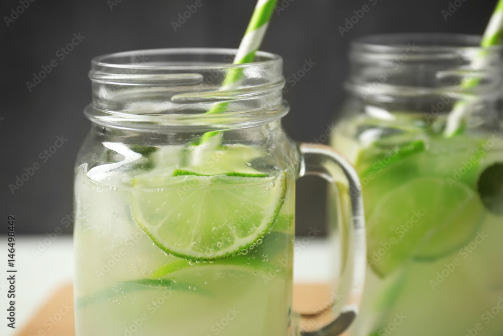 Glass jars of bracing cocktail with lime slices on dark background, closeup Glass jars of bracing cocktail with lime slices on dark background, closeup