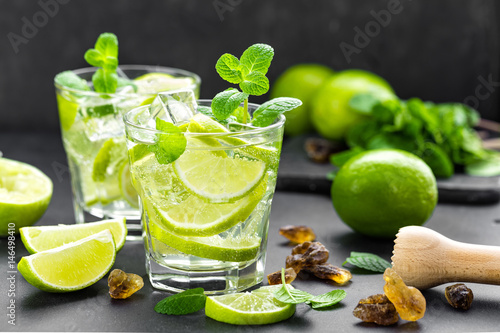 Summer mint lime refreshing cocktail mojito with rum and ice in glass on black background