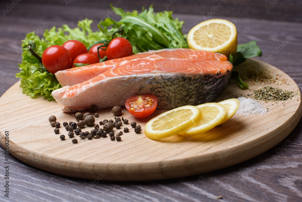 Raw salmon steaks on the wooden board. Lettuce leaves, spices, lemon slices on a wooden board. Woody background.