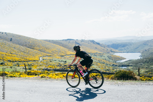 Female cyclist dressed in all black riding bicycles through the green and yellow rolling hills long shade and bright white light.
