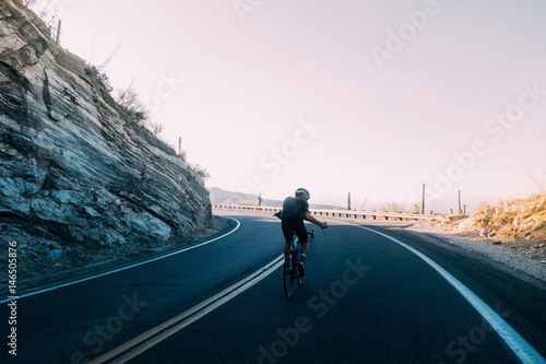 Youthful cyclist in shadow approaching the white light of morning rays while making photo as he climbs, pedals up mount lemmon in tucson, arizona, usa.