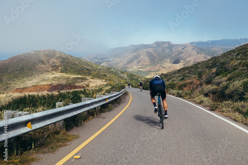 Group of cyclists, teammates, friends, descending windy narrow road next to the bay with fog and water and blue skys san francisco in norhtern california.