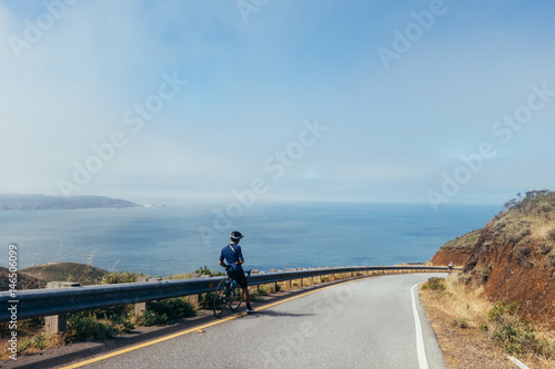 Fototapeta Naklejka Na Ścianę i Meble -  Group of cyclists, teammates, friends, descending windy narrow road next to the bay with fog and water and blue skys san francisco in norhtern california.