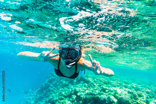 Woman with mask snorkeling in clear sea water with victory sign