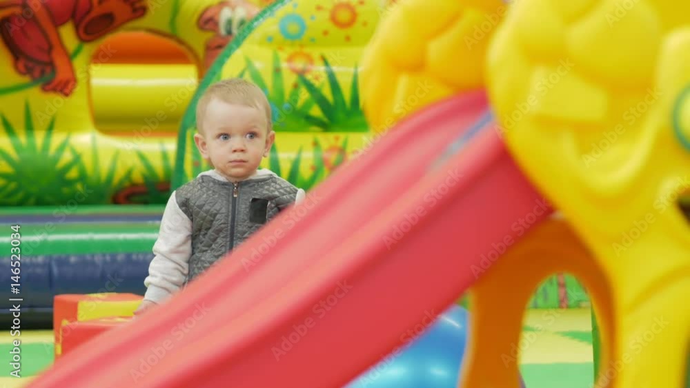 A cute kid is standing near a red slide in an amusement park A cute kid is standing near a red slide in an amusement park