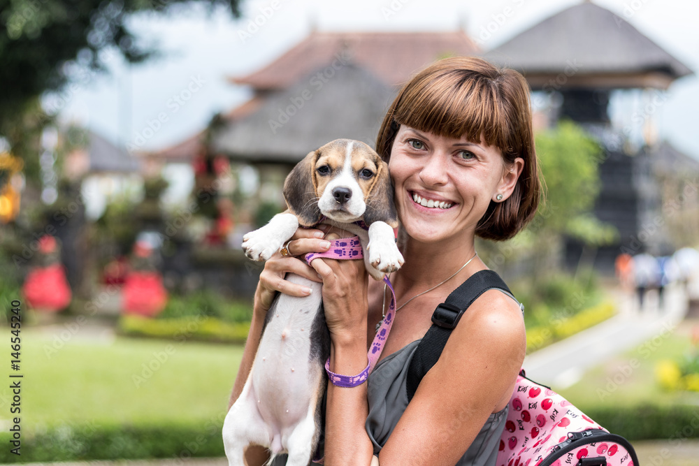 Woman beautiful young happy with poppy beagle holding a dog in her hands. Balinese temple backgorund. Indonesia, Bali. Woman beautiful young happy with poppy beagle holding a dog in her hands. Balinese temple backgorund. Indonesia, Bali.