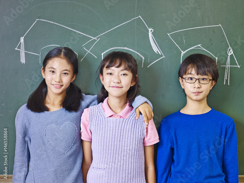 Photography asian elementary school students standing underneath chalk-drawn doctoral hats
