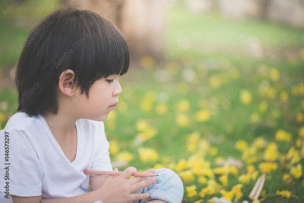Little Asian boy sitting under the tree and drawing in notebook at park Little Asian boy sitting under the tree and drawing in notebook at park