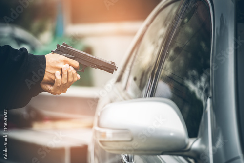 A robber dressed in black pointing a gun at a driver in a car. Car thief concept.