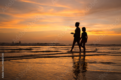 silhouette of mother and child walking on the tropical beach sunset background