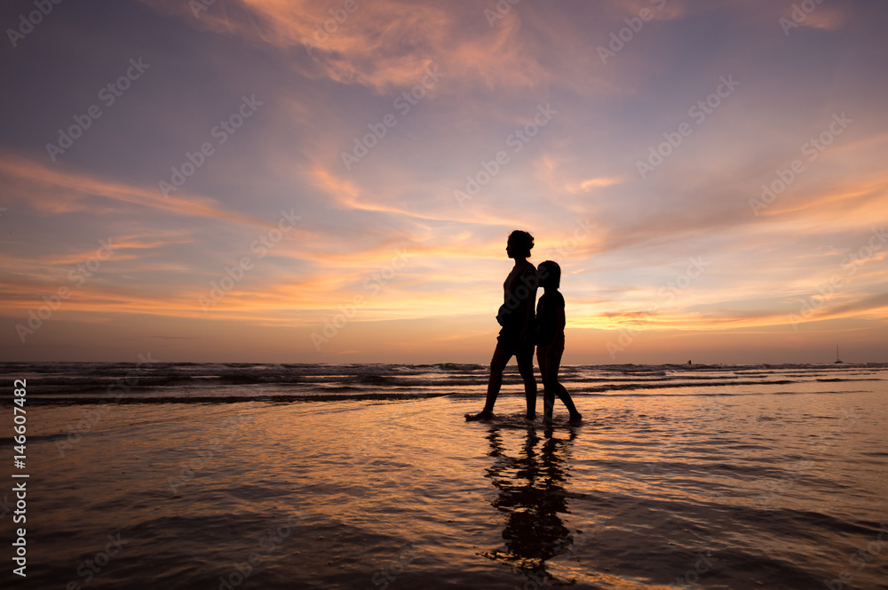 silhouette of mother and child  walking on the tropical beach  sunset background