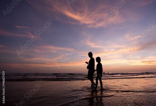 silhouette of mother and child walking on the tropical beach sunset background