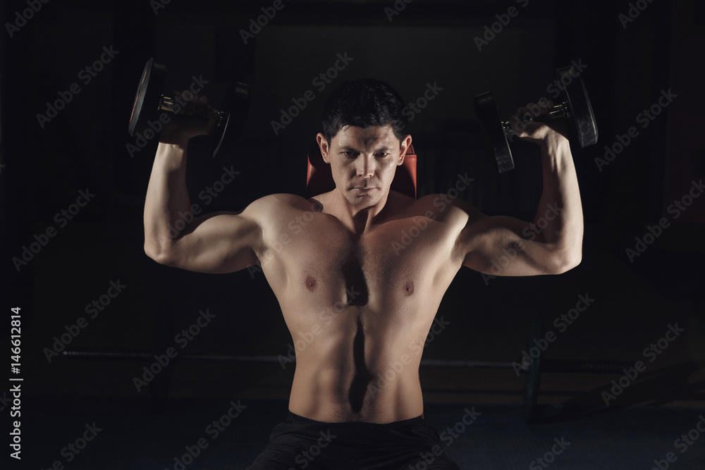 Muscular man training his shoulders with dumbbells.